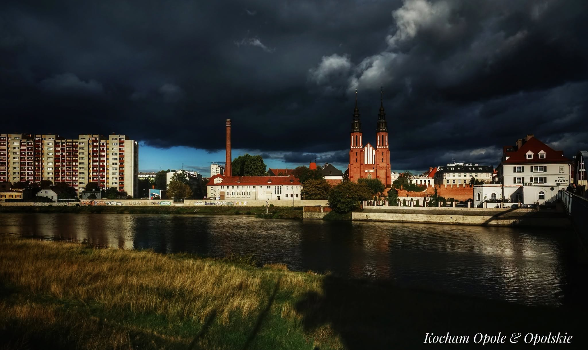Panorama Opola nad Odrą pod burzowymi chmurami, z podpisem Kocham Opole & Opolskie.